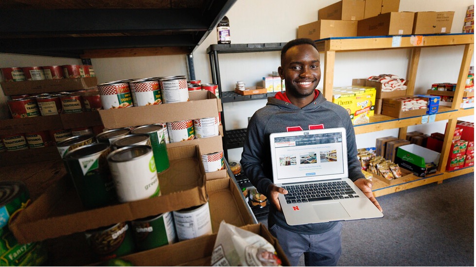 Gabin Kundwa holds his laptop to show his work in helping s Connection Point's food bank keep track of its clients by writing software that replaced handwritten note cards.