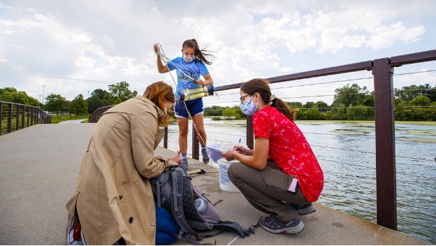 Malayna Wingert, a sophomore biological system engineering major from Sterling, Nebraska, lifts a water sample out of Holmes Lake as Anni Poetz and Maddie Carpenter record data in August 2020. 